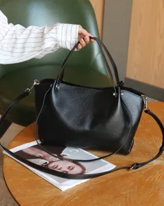 Close-up detail of black genuine leather tote handbag with pebbled texture and metal hardware.