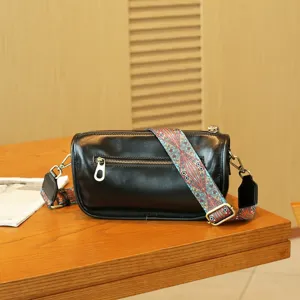 Detailed shot of a black genuine leather pillow bag with a colorful wide strap and metal zippers.
