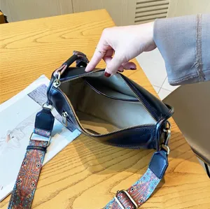 Leather pillow shoulder bag with colorful wide strap, showing interior zipper pocket and lining.