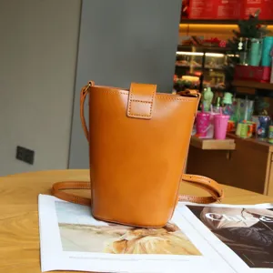 Detail view of brown leather bucket bag resting on wooden table with magazine prop.