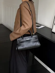Detail view of black genuine leather horizontal shoulder bag with metal lock detail and strap.