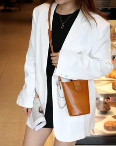 Detail view of brown leather crossbody bucket bag worn with chic blazer outfit in store.
