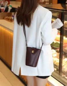 Detailed view of genuine leather crossbody bucket bag worn with chic white blazer in cafe.