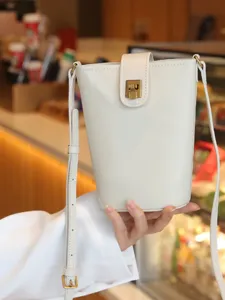 Minimalist white leather bucket bag with metal lock closure, versatile crossbody bag for women.