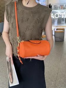Genuine leather orange cylinder crossbody bag with stylish beaded pendant for women.