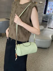 Leather cylinder shoulder crossbody bag for women, stylish green cosmetic bag with charms.
