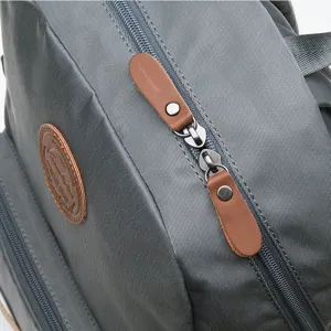 Grey nylon backpack detailed view with durable zippers, leather pull tabs, and classic patch.