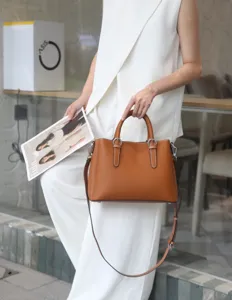 Gros plan d'un sac cabas en cuir marron élégant avec bandoulière tenu par un mannequin.