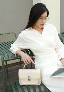 White leather top handle handbag detail, minimalist structured design with metal lock closure.