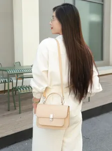 Detail shot of beige leather crossbody bag, showing texture, metal clasp and shoulder strap.