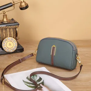 Dettaglio borsa a tracolla in pelle verde scuro con doppia chiusura lampo e tracolla.