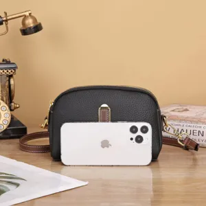 Dettaglio della borsa a tracolla in pelle nera, dimensioni compatte mostrate con smartphone.