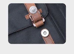 Black canvas backpack detail showcasing brown leather strap and metal magnetic snap closure.