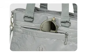 Grey nylon tote bag detail close-up showing front zipper pocket and metal hardware rings.