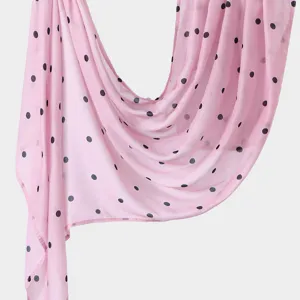 Close-up detail of lightweight pink long scarf with classic black polka dots draped gracefully.