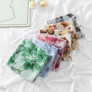 Close-up detail shot of stacked floral butterfly printed scarves showcasing soft voile fabric texture.