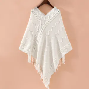 Close-up details of the white knitted poncho featuring elegant tassels and textured geometric pattern.