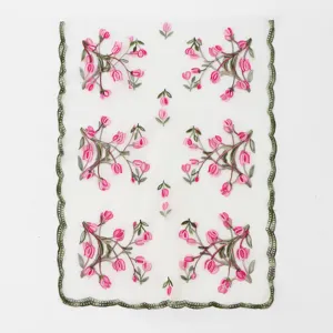 Gros plan sur la broderie florale rose délicate et le bord festonné vert sur tissu transparent.