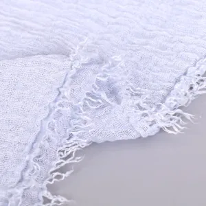 Close-up detail of light blue crinkled cotton linen scarf showing soft frayed edge texture.