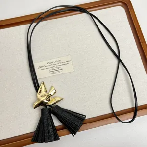 Detailansicht der schwarzen Lederband-Halskette mit goldenem Vogelanhänger und Quasten.