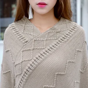 Detailed view of women's beige knit poncho sweater with geometric textured pattern.
