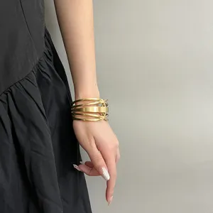 Vista detallada de un brazalete rígido geométrico y calado en oro para mujer elegante.