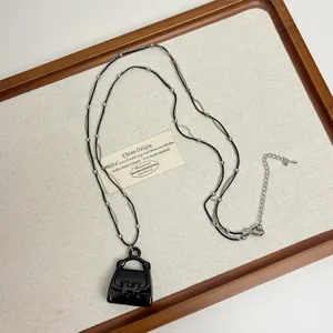 Close-up details of the multi-layer necklace with a black handbag pendant on wooden tray.