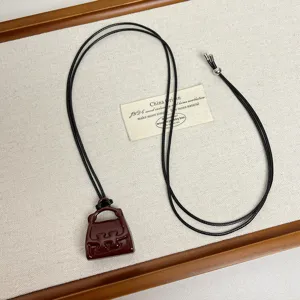 Detail view of miniature handbag pendant necklace featuring black cord on textured backdrop.