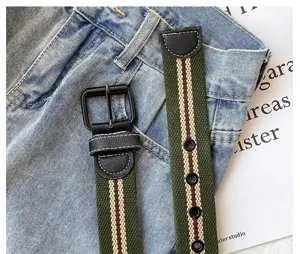 Canvas belt detail view, green striped webbing with black leather and metal buckle.