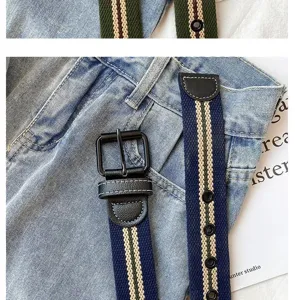 Detail shot of a striped canvas belt with leather trim and black buckle on denim jeans.