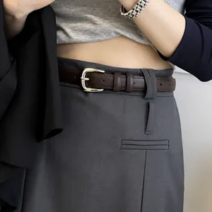 Close-up detail of women's brown leather belt with silver metal buckle worn on grey pants.