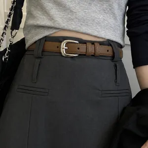 Minimalist genuine leather women's belt closeup, slim brown strap with silver metal buckle.