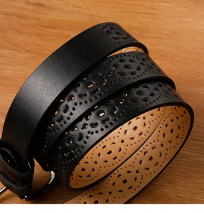 Close-up detail of black leather belt featuring intricate hollow carved floral perforated patterns.