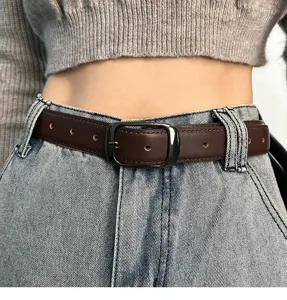 Detail view of a retro brown leather belt with metal pin buckle worn on blue denim jeans.