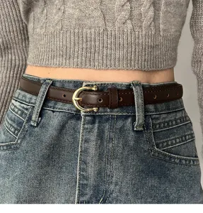Primo piano dettagliato di una sottile cintura in pelle marrone con fibbia dorata sui jeans.