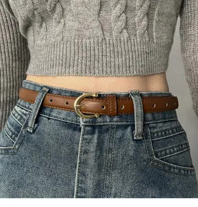 Primo piano dettagliato di una sottile cintura in marrone con fibbia dorata e jeans.