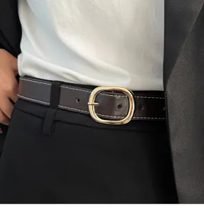 Brown leather belt detail shot featuring a gold oval buckle and white contrast stitching.