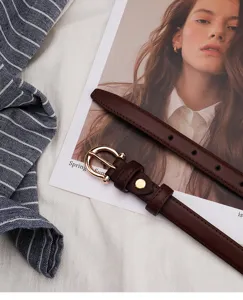 Detail shot of a minimalist brown thin leather belt with a shiny gold round buckle.