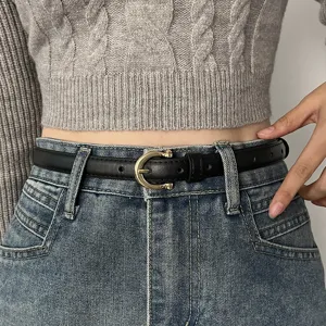 Sottile cintura in pelle nera con fibbia dorata a ferro di cavallo per look casual.