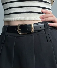 Close-up detail of women's black leather belt with gold metal pin buckle worn on pants.