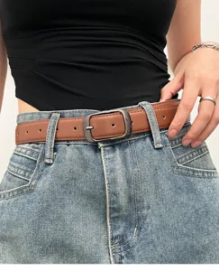 Detail shot of a stylish brown leather belt with metal buckle worn over classic denim jeans.