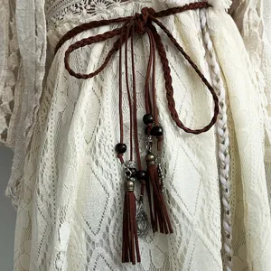Détail de ceinture en corde tressée marron style bohème, avec glands et perles de bois.