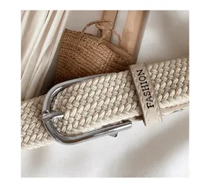 Close-up of beige woven elastic belt with silver buckle and fashion letter print detail.