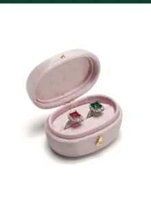 Close-up of pink velvet oval ring box with dual slots, displaying elegant gemstone rings inside.