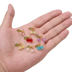 Close-up of colorful glass cherry charms with green leaves and gold loops for DIY jewelry.