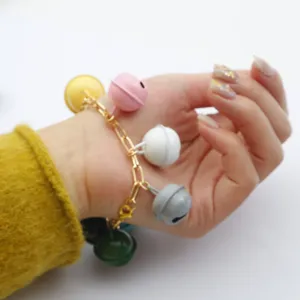 Detailaufnahme des bunten Glocken-Armbands mit lackierten Anhängern an goldener Kette.