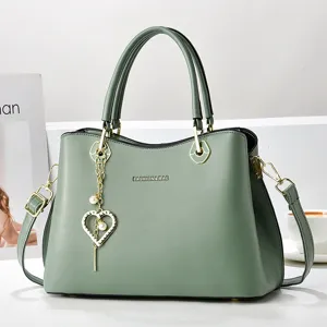 Green leather shoulder bag detail, stylish tote with heart charm and metal hardware.