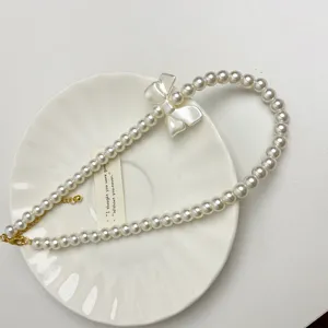Close-up van elegante parelketting met chique strikhanger en delicate metalen kettingdetails.