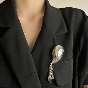 Close-up view of the metallic streamlined tassel brooch, showcasing fine chains and smooth finish.