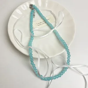 Detailopname van de lichtblauwe kraal choker ketting met schattige witte lintstrik accenten.